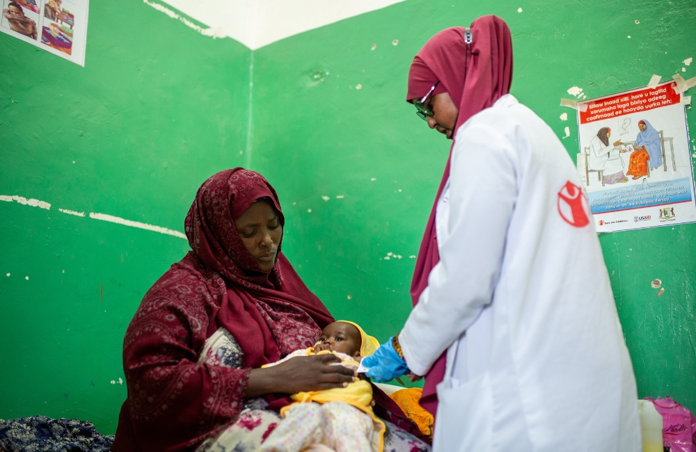 As mum cradles her baby, a health worker gives medical treatment